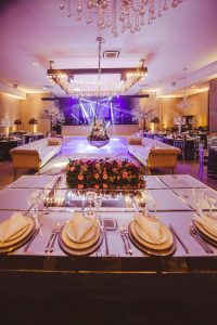 Luxurious banquet hall setup with chandeliers and floral centerpiece, ideal for weddings.